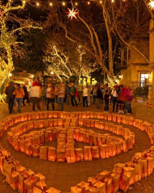 A festive scene at night with people gathered around a circular arrangement of glowing paper lanterns.