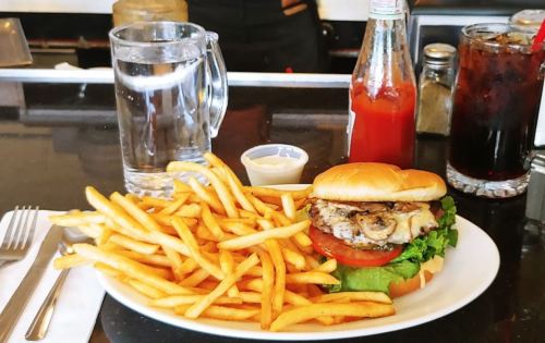 A plate with a burger topped with lettuce, tomato, and mushrooms, served with a side of fries and drinks.