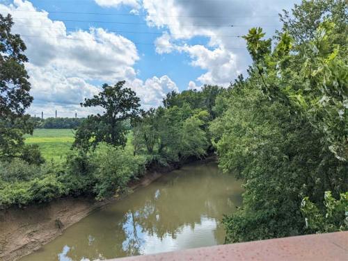 A serene river flows through lush greenery under a partly cloudy sky.