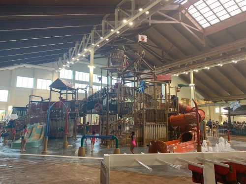 Indoor water park featuring a large play structure with slides, water features, and children playing in the water.