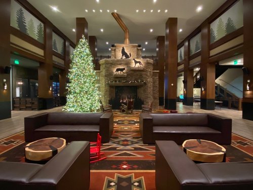 Cozy lobby with a large Christmas tree, stone fireplace, and dark leather seating, surrounded by rustic decor.