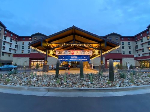 Entrance of Great Wolf Lodge, featuring a large sign and festive lights, surrounded by landscaping and a cloudy sky.