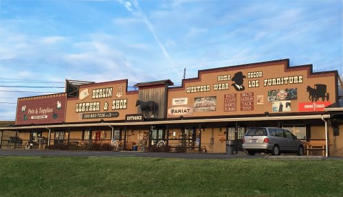 A rustic storefront featuring signs for Berlin Leather & Shoe, with western decor and log furniture displayed outside.