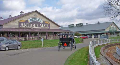 A view of Berlin Antique Mall with a horse-drawn carriage in the foreground and craft mall buildings in the background.