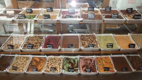 A display case filled with various types of fudge, labeled with names, in an assortment of colors and textures.