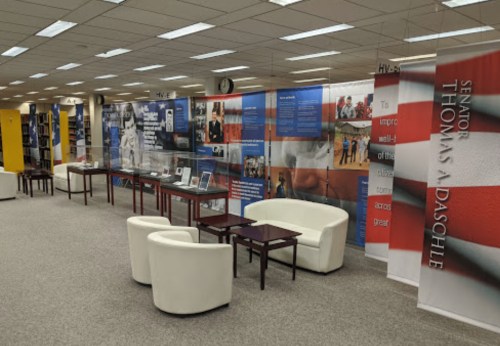 A modern library space featuring white seating, display cases, and informational banners about health and wellness initiatives.