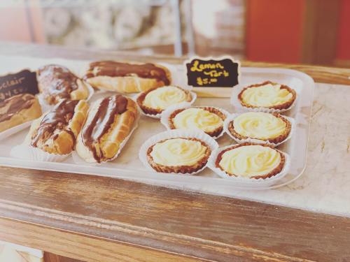 A tray of pastries featuring chocolate eclairs and lemon tarts with creamy frosting, displayed on a wooden counter.