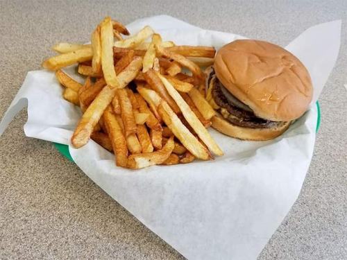 A plate of golden fries next to a hamburger on a bun, served on a white paper-lined tray.