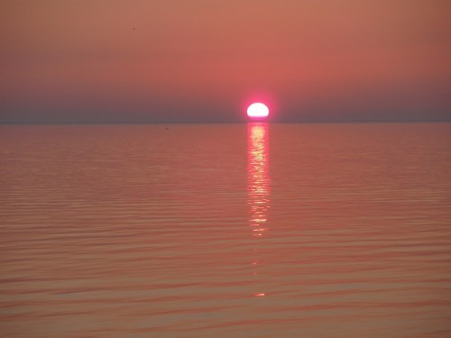 A vibrant sunset over calm waters, with the sun reflecting on the surface, creating a serene atmosphere.