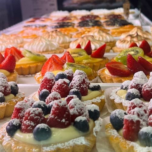 A display of colorful pastries topped with fresh fruit and powdered sugar, featuring strawberries, blueberries, and kiwi.
