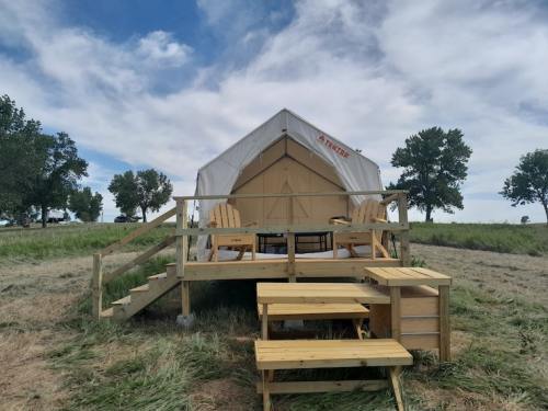 A glamping tent on a wooden deck, surrounded by grass and trees, with seating and a picnic table in front.