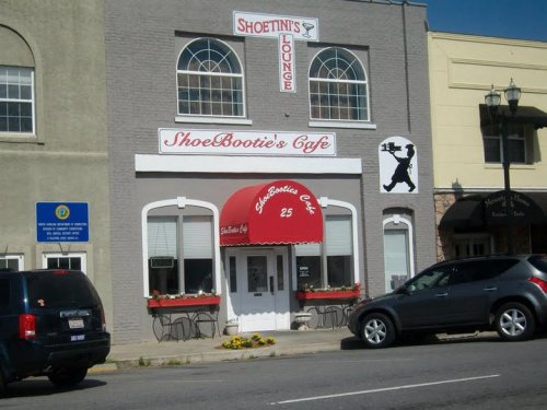 Exterior of ShoeBootie's Cafe with red awnings, a sign for Shoetini's Lounge, and parked cars in front.