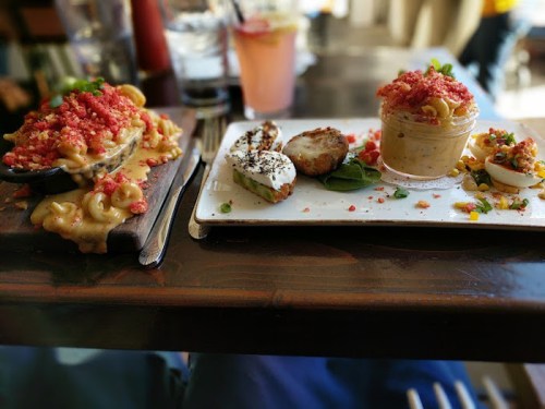 A table with two plates: one with mac and cheese topped with crushed snacks, the other with various small dishes and a dessert.