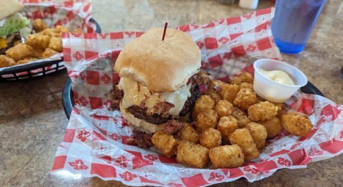 A hearty burger with melted cheese on a bun, served with crispy tater tots and a side of dipping sauce.