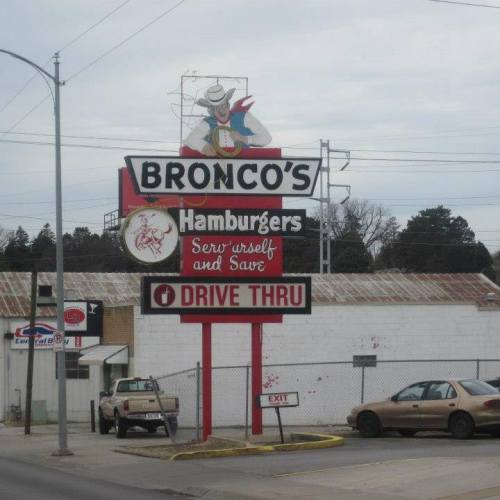 Sign for Bronco's Hamburgers featuring a cowboy mascot, with "Drive Thru" and "Serve Yourself and Save" messages.