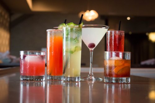 A variety of colorful cocktails in glasses on a bar counter, including a martini and several mixed drinks.