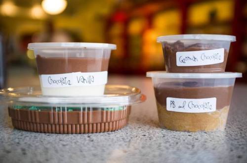 Three containers of dessert: chocolate vanilla, German chocolate, and peanut butter chocolate, on a countertop.