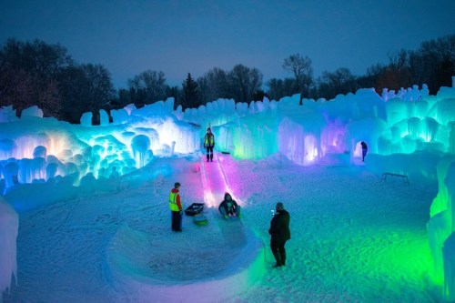 Colorful ice formations illuminated at night, with people enjoying activities in a snowy landscape.