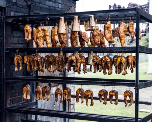 A metal rack displaying various types of smoked fish hanging in a rustic setting.