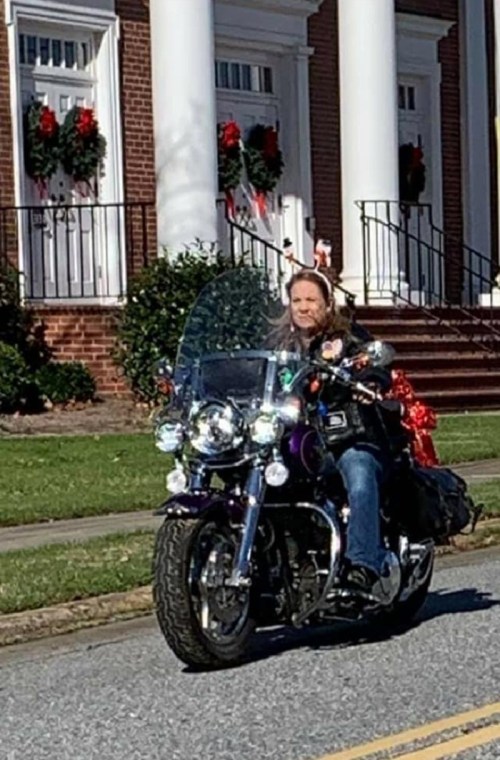 A person riding a motorcycle decorated with festive items, passing by a building adorned with holiday wreaths.