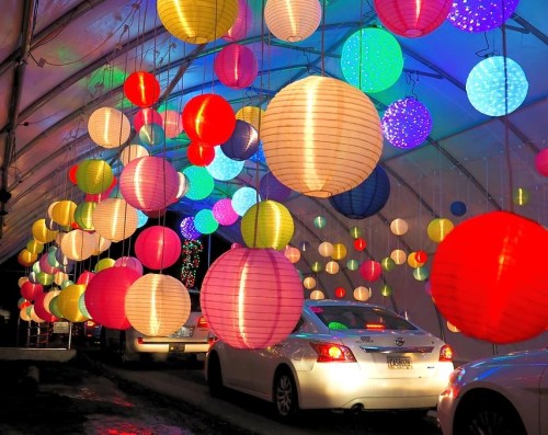 Colorful lanterns hang from a tent, illuminating cars below in a festive, vibrant display.