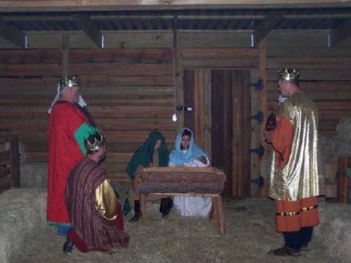 A nativity scene with figures in traditional costumes gathered around a manger in a rustic setting.