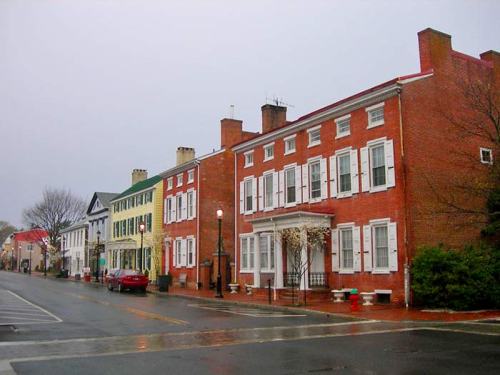 Historic brick buildings line a rainy street, with colorful facades and a few trees in the background.