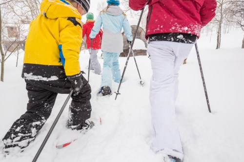 A group of people in colorful winter clothing walking through deep snow with ski poles. Snow-covered trees in the background.