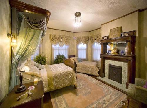 Cozy bedroom with two beds, elegant decor, large windows, and a decorative fireplace. Soft lighting enhances the ambiance.