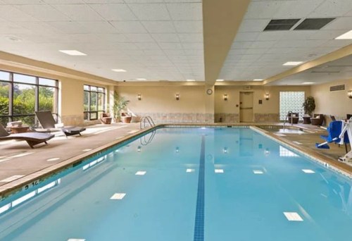 Indoor swimming pool with lounge chairs, large windows, and soft lighting.