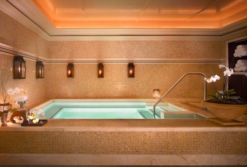 A serene spa room featuring a small, illuminated hot tub surrounded by elegant tile and soft lighting.