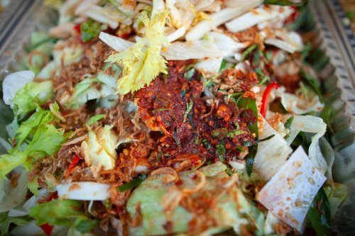 A vibrant salad topped with herbs, spices, and crispy toppings, served in a decorative tray.
