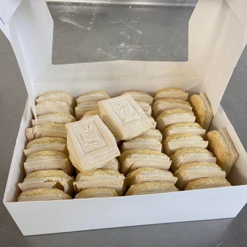 A white box filled with neatly arranged, light-colored layered cookies.