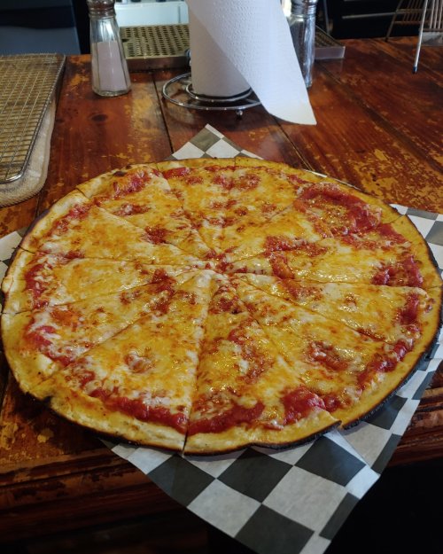 A freshly baked cheese pizza sliced into 16 pieces, served on a checkered paper in a rustic wooden setting.