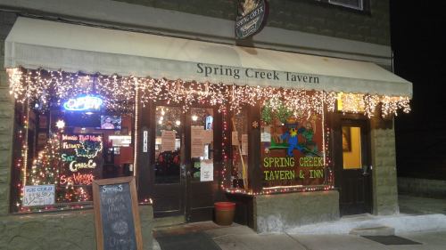Exterior of Spring Creek Tavern, adorned with string lights, featuring a colorful sign and an open door.