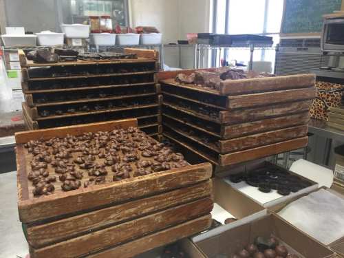 Stacks of wooden trays filled with various types of chocolate confections in a kitchen setting.
