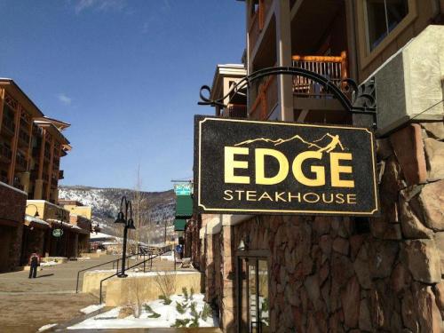 Sign for "EDGE Steakhouse" hanging outside a building, with snow-capped mountains in the background and a clear blue sky.