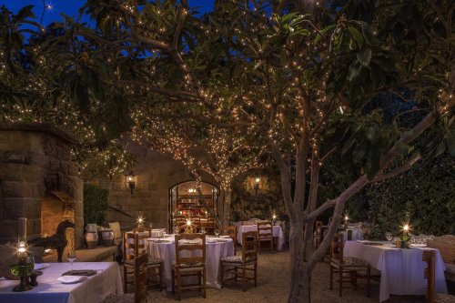 A beautifully lit outdoor dining area with tables, chairs, and twinkling lights among trees at dusk.