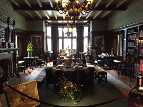 A vintage room with ornate furniture, bookshelves, and a decorative vase, illuminated by natural light.