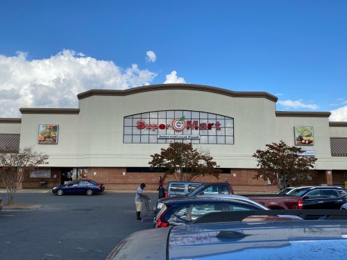 Exterior of Super Mart grocery store with a clear blue sky and parked cars in front.