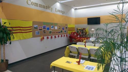 A community lounge decorated with yellow and red banners, photos, and a table set with yellow cloth and chairs.