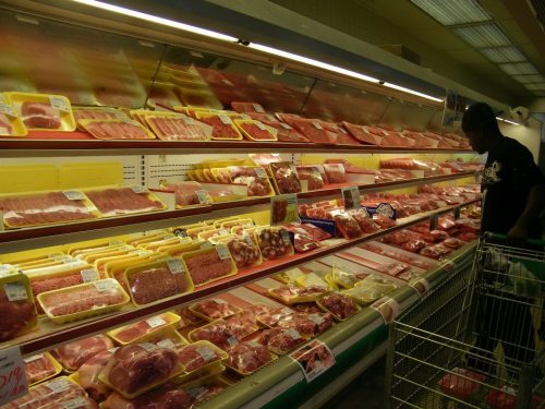A grocery store meat section with various packaged meats and a person browsing the selection.