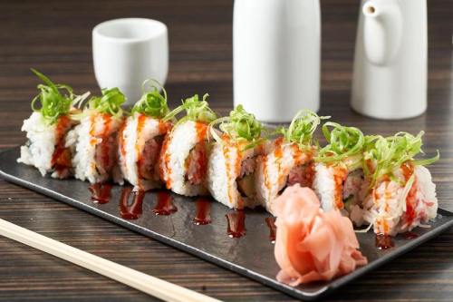 A platter of sushi rolls topped with green onions, accompanied by pickled ginger and soy sauce on a dark wooden table.