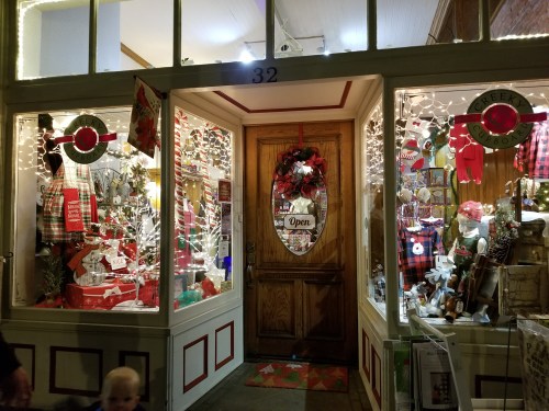 A festive shop window decorated with holiday lights, gifts, and seasonal decor, featuring an "Open" sign.