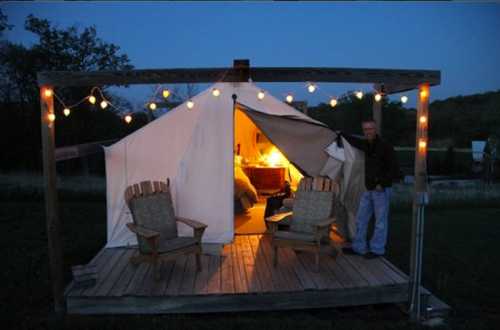 A cozy tent on a wooden deck at dusk, with string lights and two chairs outside, inviting warmth from inside.