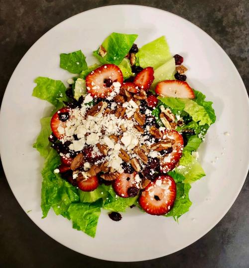 A fresh salad with romaine lettuce, strawberries, nuts, and feta cheese on a white plate.