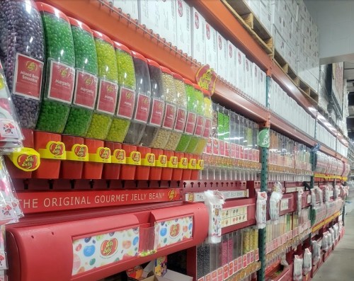 A colorful display of various jelly bean flavors in clear containers on shelves at a candy store.