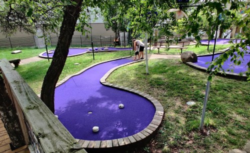 A mini-golf course with purple turf, featuring winding paths and a player preparing to take a shot.