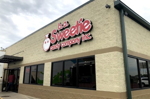 Exterior of b.a.b. Sweetie Candy Company Inc. building with a colorful sign and large windows.
