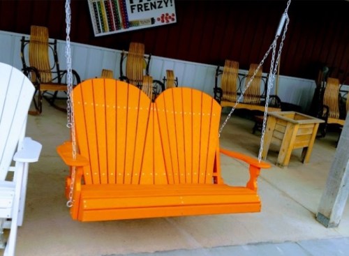 A bright orange wooden swing with a heart-shaped backrest, hanging from chains in a rustic setting.